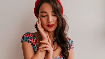 Woman with loose wavy hair wearing red hat, red lipstick, and floral top.