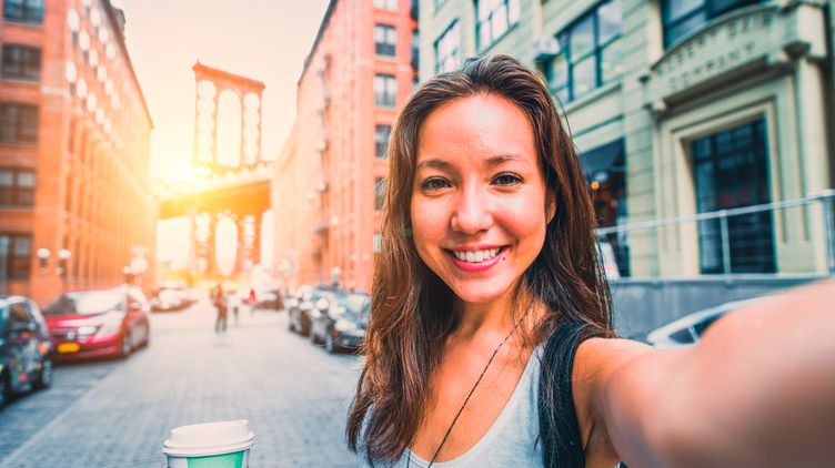 Woman taking selfie with Brooklyn Bridge in the background.