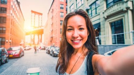 Woman taking selfie with Brooklyn Bridge in the background.
