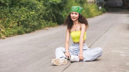 A young woman wearing a green bandana, yellow tube top, and jeans. 