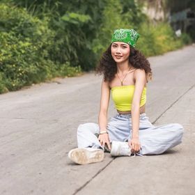 A young woman wearing a green bandana, yellow tube top, and jeans. 