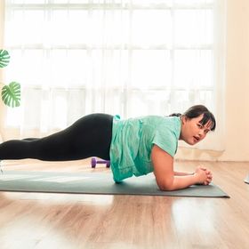 Plus-sized Asian woman doing planks at home with tablet.
