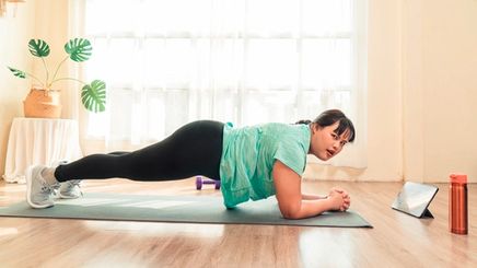 Plus-sized Asian woman doing planks at home with tablet.