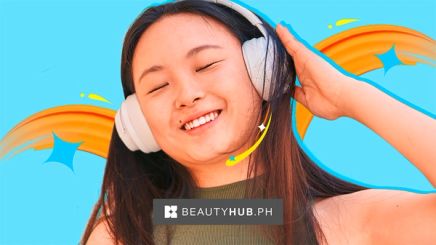 Asian woman in a green halter top listening to music through white headphones.