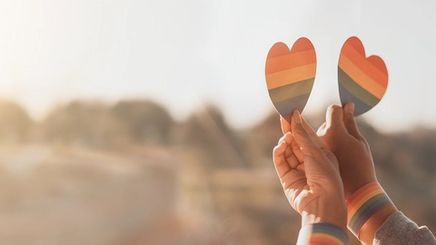 Two hands holding rainbow hearts