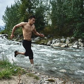 Fit Asian man running in rocky creek while shirtless.