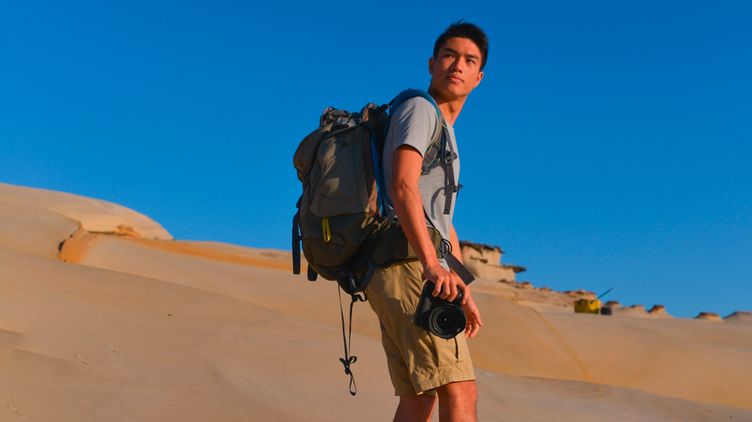Asian man with a backpack and a camera in the desert.