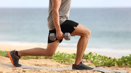 Cropped photo of man doing lunges with barbels on the beach.