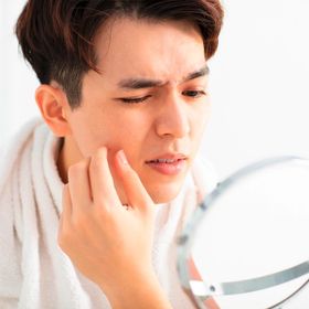 A portrait man squeezing his pimple in front of a mirror.