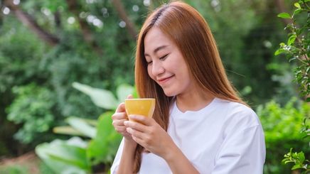 A woman in a white shirt smiling while looking at her cup of coffee.