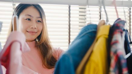 Asian woman with ombre hair and pink shirt looking through closet