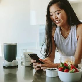 Asian woman leaning on kitchen counter texting.