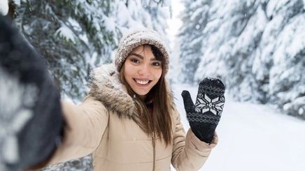 Asian woman in winter wear, smiling against a snowy backdrop in nature