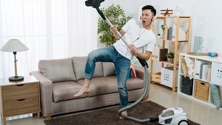 Asian man being playful while cleaning the house with a vacuum. 