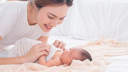 Asian mom looking at newborn on bed