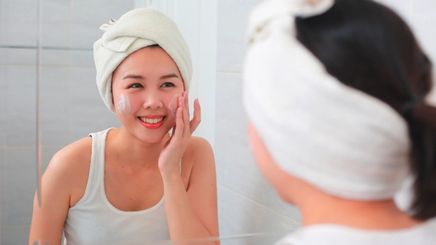 Asian woman applying moisturizer on your face in the bathroom.