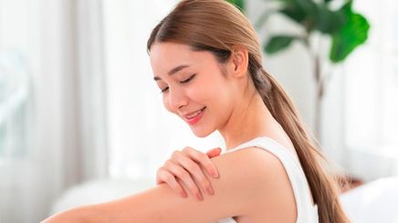 Smiling woman applying cream on her upper arm
