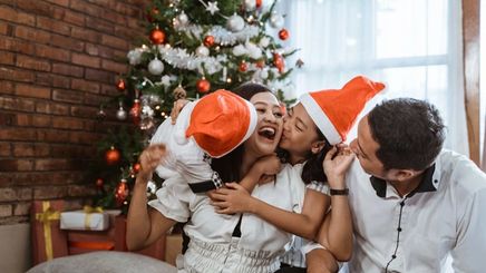 Asian kids kissing mom in front of Christmas tree while dad looks on.