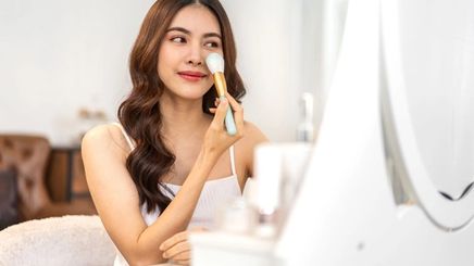 Asian woman applying makeup on cheeks