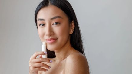 Asian woman with healthy lips, holding a lip balm.