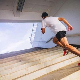 A man with toned, muscled legs sprinting up a flight of stairs.