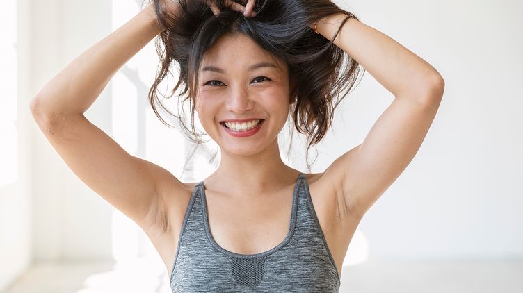 Smiling Asian woman with arms raised and holding hair up