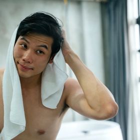 An Asian man rubbing a towel on his hair and looking at himself in the mirror