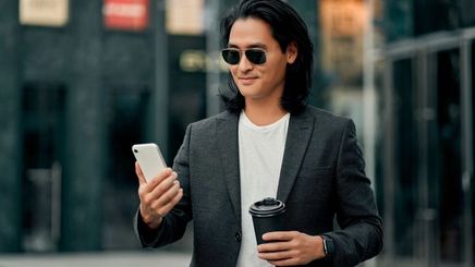 Asian man with long, healthy hair wearing sunglasses, holding his phone and coffee
