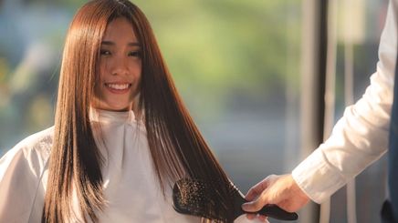 Asian woman smiling at a salon with styled straight hair.