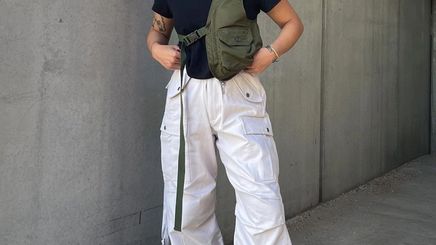 Woman wearing gorpcore outfit with white cargo pants, sunglasses, vest, and sneakers.