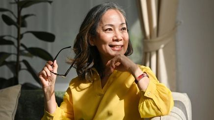 Asian woman with medium-length, wavy brown hair wearing a yellow shirt