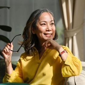 Asian woman with medium-length, wavy brown hair wearing a yellow shirt