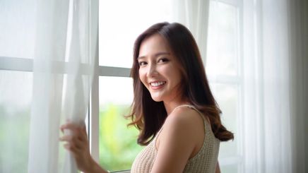 Beautiful Asian woman opening the window and smiling at the camera