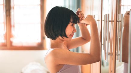 Woman looking at bangs and trimming them in front of mirror.