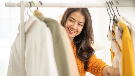 Asian woman wearing yellow sweater, looking at clothes