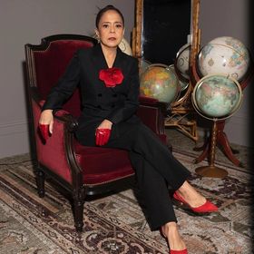 Actress Dolly De Leon sitting wearing black suit with red details.