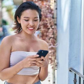 Woman with short hair wearing a white tube top, texting.