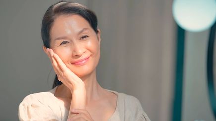 Smiling mature Asian woman with one hand on the side of her face.