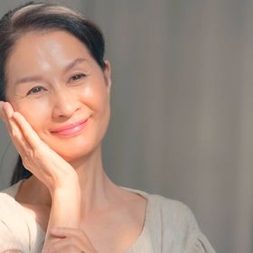 Smiling mature Asian woman with one hand on the side of her face.