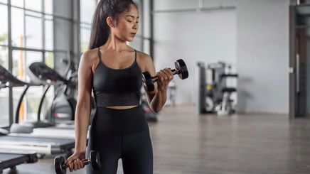 An athletic Asian woman lifting weights at the gym.