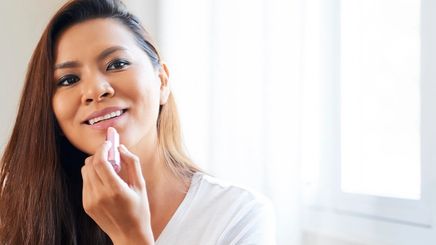 Smiling Asian woman applying pink lipstick