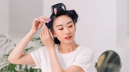 Asian woman wearing hair rollers to curl her hair.