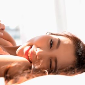 A portrait of woman winking while lying on a bed, sunlight hitting her skin.