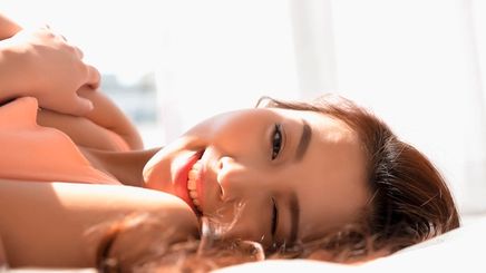A portrait of woman winking while lying on a bed, sunlight hitting her skin.