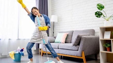 Asian woman happily dancing with a mop and a bucket of house cleaning products. 
