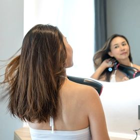 Asian woman using a blow dryer in front of a mirror.