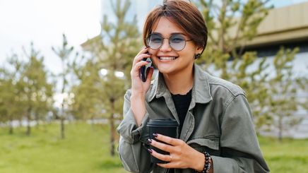 Asian woman with short hair wearing sunglasses, holding a phone and coffee cup.