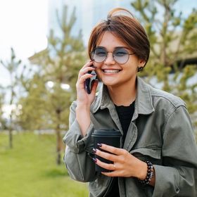 Asian woman with short hair wearing sunglasses, holding a phone and coffee cup.