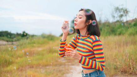 Asian woman in a striped shirt blowing bubbles outdoors.
