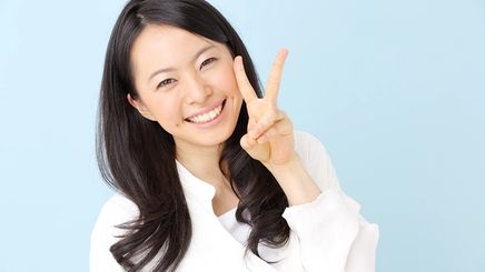 Smiling Asian making the peace sign against blue background